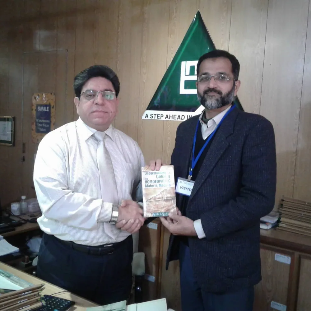 Dr. Mir Zahed shaking hands with Dr. Aman Ullah Bismil as he presents him a copy of the book.