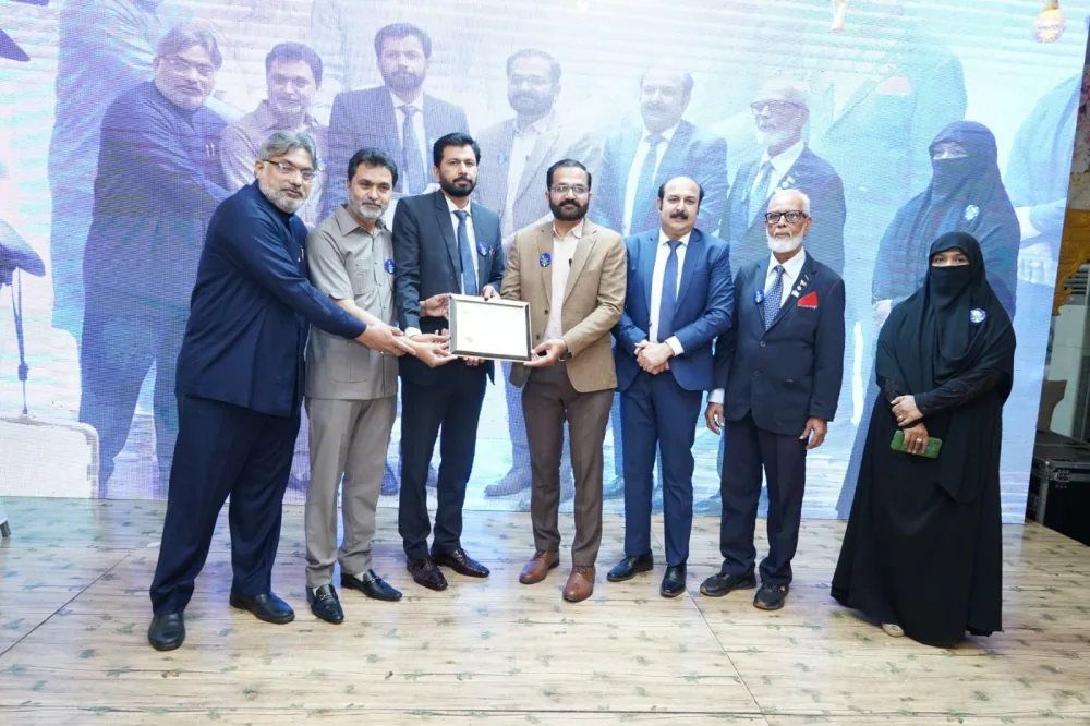 Dr. Mir Zahed, in a tan jacket, receiving a framed certificate held by three other men, with three more people standing beside them before a large screen.