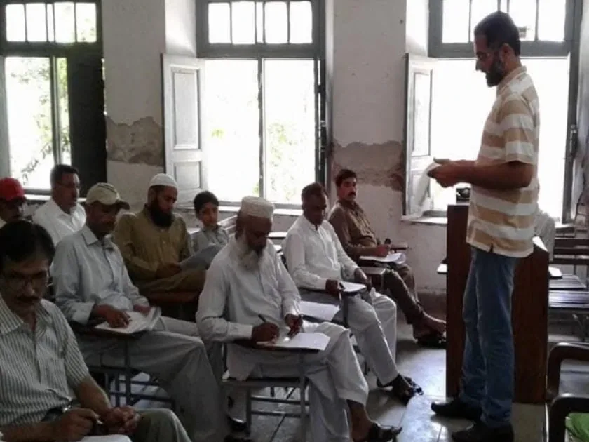 Dr. Mir Zahed standing at the front of a classroom, teaching doctors who take notes at their desks.